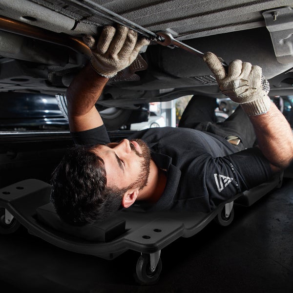 Mechaniker benutzt eine Werkstattliege unter einem Auto für Reparaturen