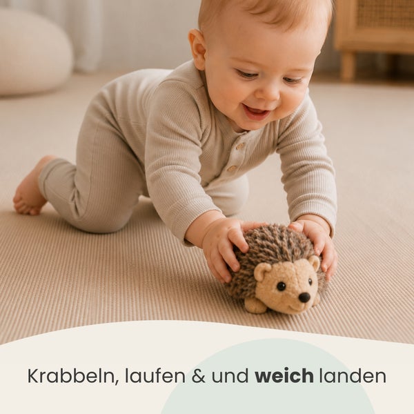 Kleinkind krabbelt auf einer weichen Spielmatte und spielt mit einem Stoffigel.