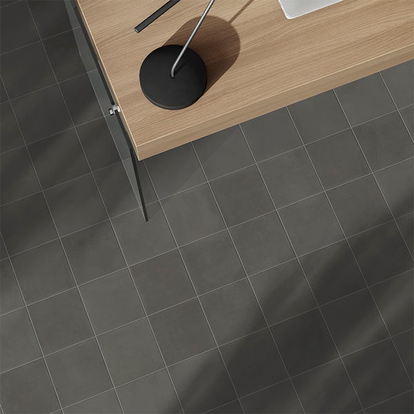 Draufsicht auf quadratische Bodenfliesen in Betonoptik mit einem Holztisch und einer Schreibtischlampe im modernen Innenraum.