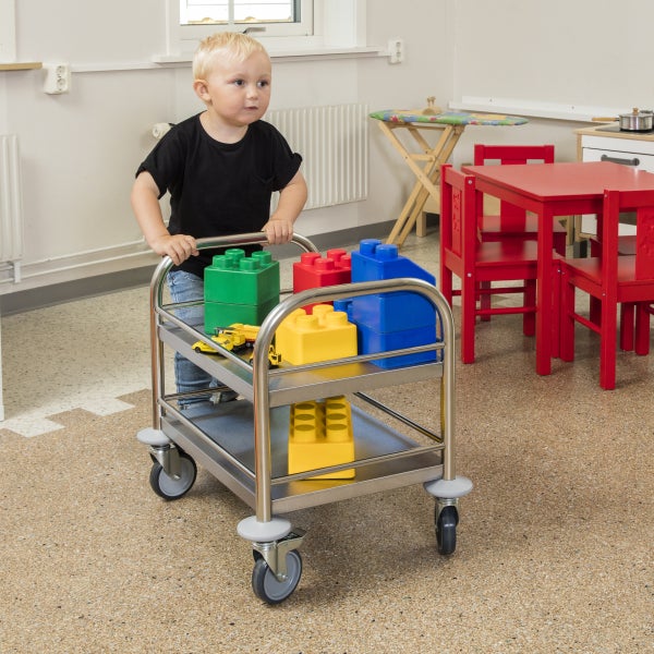 Junge schiebt Servierwagen mit Spielzeug im Kinderzimmer