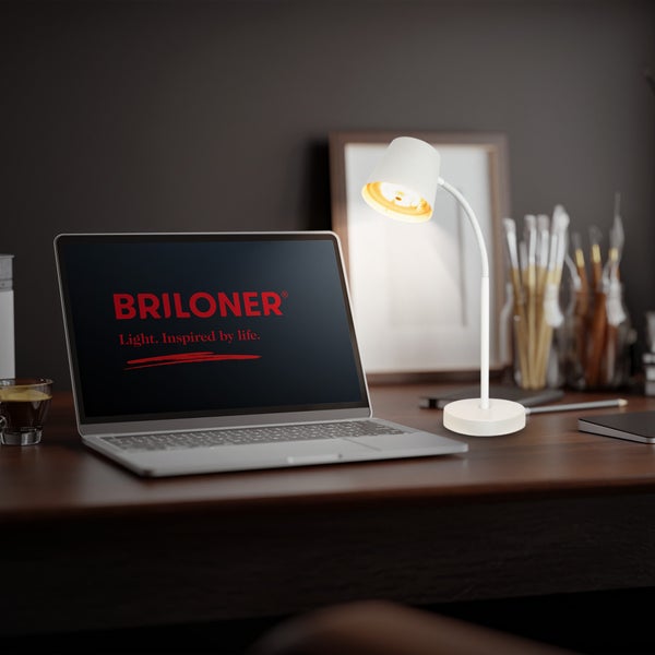Weiße Schreibtischlampe mit flexiblem Arm auf einem dunklen Schreibtisch neben einem Laptop mit Briloner Logo.