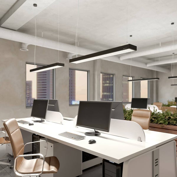 Modernes Büro mit rechteckigen schwarzen LED-Pendelleuchten über weißen Schreibtischen mit Computern und braunen Lederstühlen.