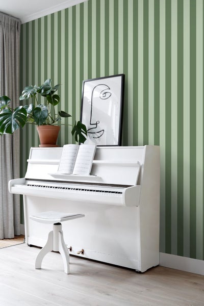 Zimmer mit gestreifter Tapete, weißem Klavier, Hocker, Zimmerpflanze und gerahmtem Bild