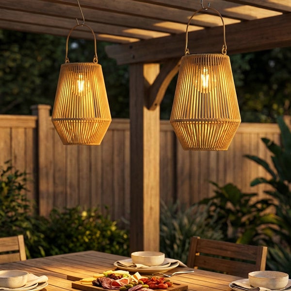Zwei hängende Solar-Laternen aus Rattan mit warmem Licht über einem gedeckten Holztisch unter einer hellen Pergola im Garten.