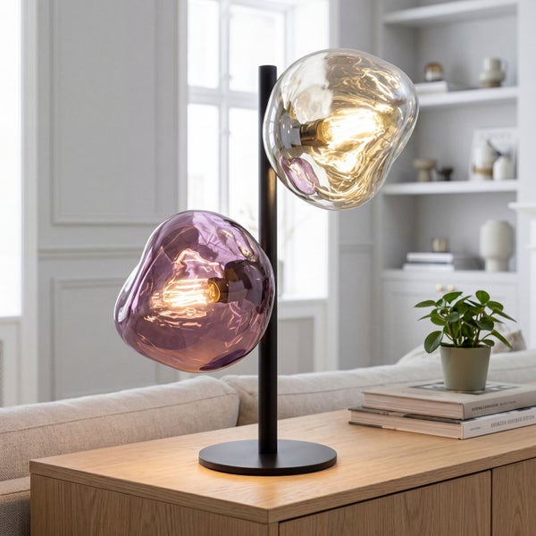 Moderne Tischleuchte mit zwei organisch geformten Glasschirmen in Violett und Bernstein auf schwarzem Metallsockel in hellem Wohnzimmer.