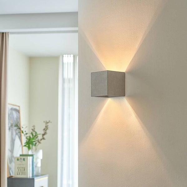Moderne würfelförmige Wandleuchte aus Beton mit Licht nach oben und unten, montiert an einer hellen Wand in einem hellen, modernen Innenraum.