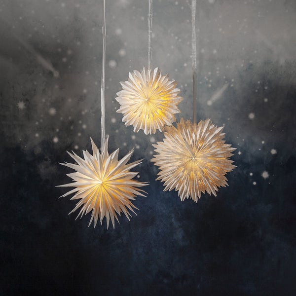 Drei Papiersterne hängen an Bändern und sind beleuchtet.