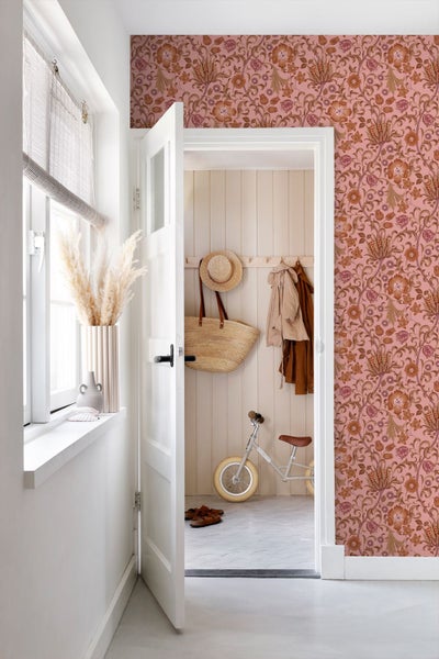 Heller Flur mit floral gemusterter Tapete, einer weißen Tür und Blick in ein angrenzendes Zimmer mit Garderobe und Kinderlaufrad.