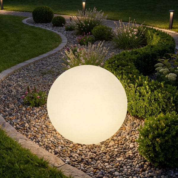 Leuchtende Gartenkugel in einem modern gestalteten Gartenbeet mit Kieselsteinen und verschiedenen Pflanzen.
