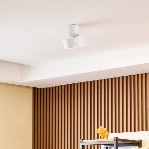 Weiße, zylindrische Deckenleuchte an einer hellen Decke montiert, im Hintergrund eine Wand mit vertikalen Holzpaneelen.