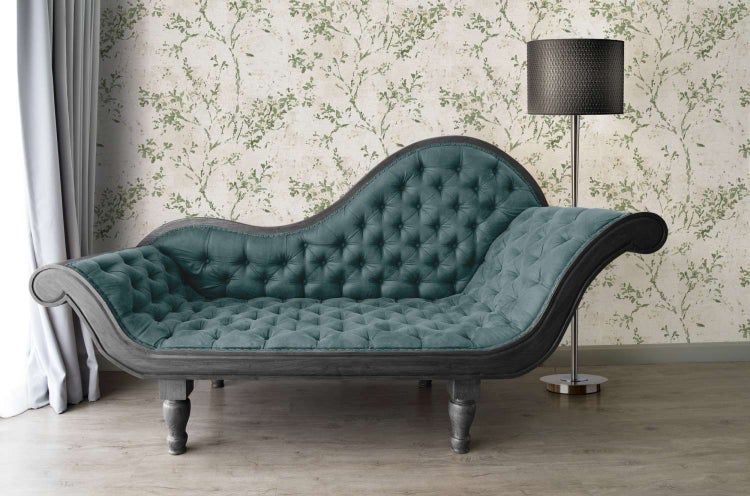 Eine Chaiselongue mit Knopfheftung steht vor einer Wand mit pflanzlichem Tapetenmuster und einer Stehlampe in einem eleganten Wohnzimmer.