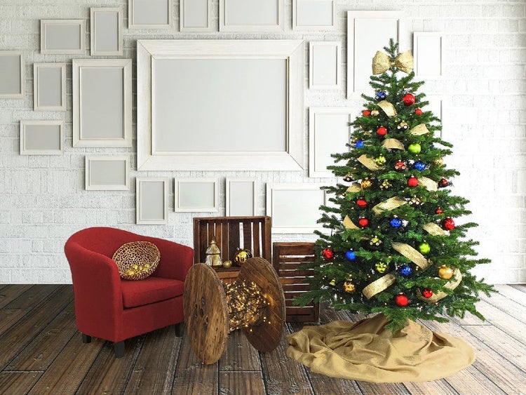 Festlich geschmückter Weihnachtsbaum mit Kugeln und Schleifen vor einer Wand mit Bilderrahmen, einem Sessel und einer hölzernen Kabeltrommel.