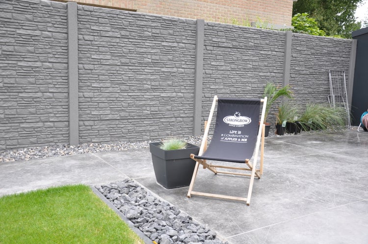 Gartenszene mit Sichtschutzzaun in Steinoptik, Liegestuhl und Bepflanzung