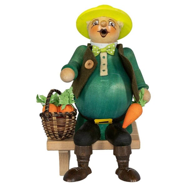 Räuchermann Gärtner aus Holz sitzt auf einer Bank mit einem Korb voll Karotten für die Osterdekoration oder als traditionelles Wohnaccessoire