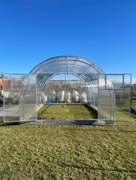 Rundbogengewächshaus mit Metallrahmen und Polycarbonat-Stegplatten, weit geöffnete Doppelflügeltüren, auf einer Rasenfläche stehend.