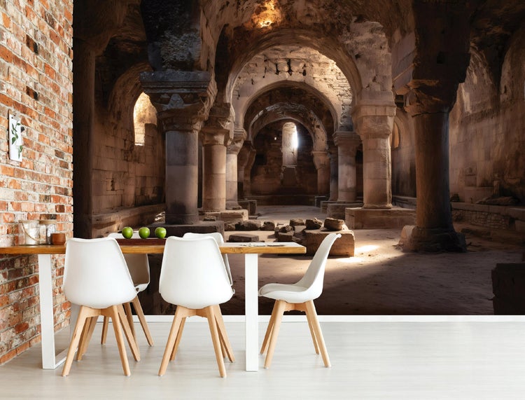 Fototapete mit antikem Steingewölbe und Säulen in einem modernen Esszimmer mit weißem Tisch, Stühlen und einer rustikalen Backsteinwand.