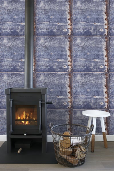 Wohnraum mit Kaminofen, Holzlagerkorb und Wandgestaltung in Metallplattenoptik