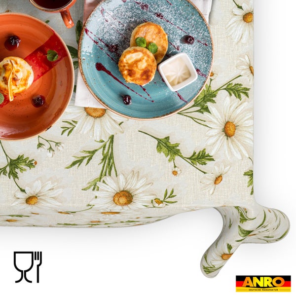 Tischdecke mit Gänseblümchen-Muster und floralem Design, dekoriert mit Tellern und Speisen. ANRO Deutsche Manufaktur Logo. Lebensmittelecht.