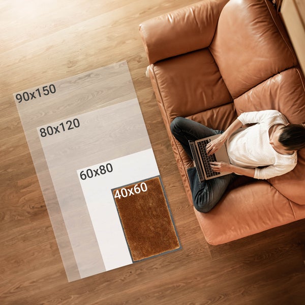 Verschiedene Größen von Fußmatten auf dem Boden, Person sitzt auf Ledersofa mit Laptop