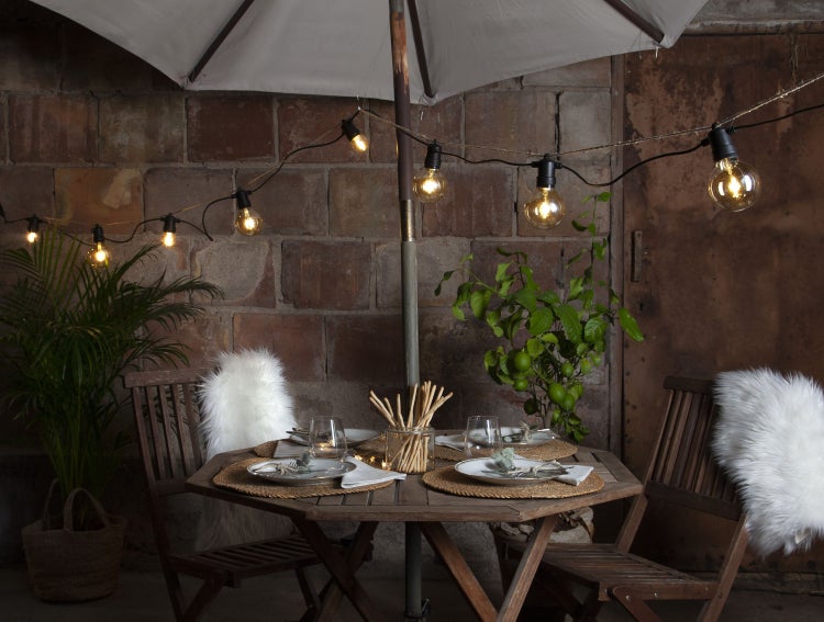 Gedeckter Gartentisch mit Sonnenschirm und Lichterkette