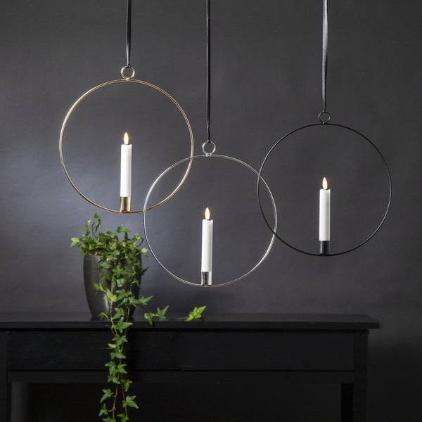 Drei runde Kerzenhalter aus Metall mit Kerzen hängen über einem Schrank.