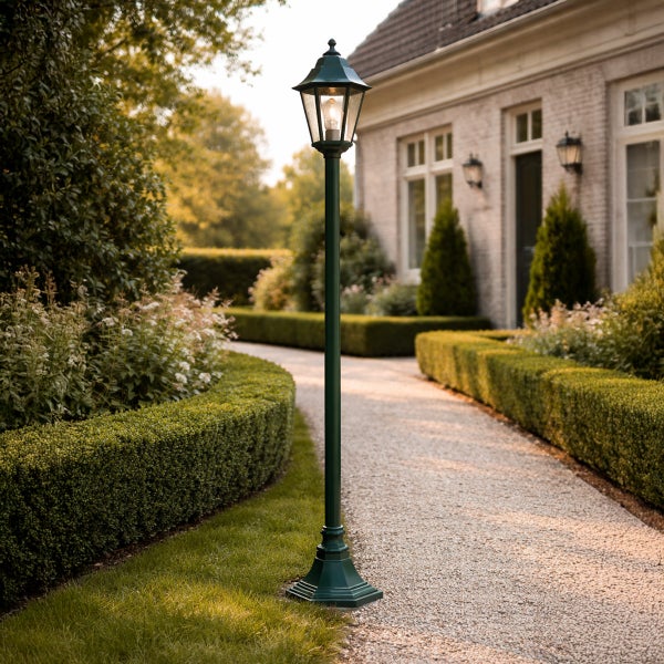 Klassische dunkelgrüne Gartenlaterne an einem Kiesweg in einem hellen, gepflegten Garten mit Hecken und Wohnhaus.