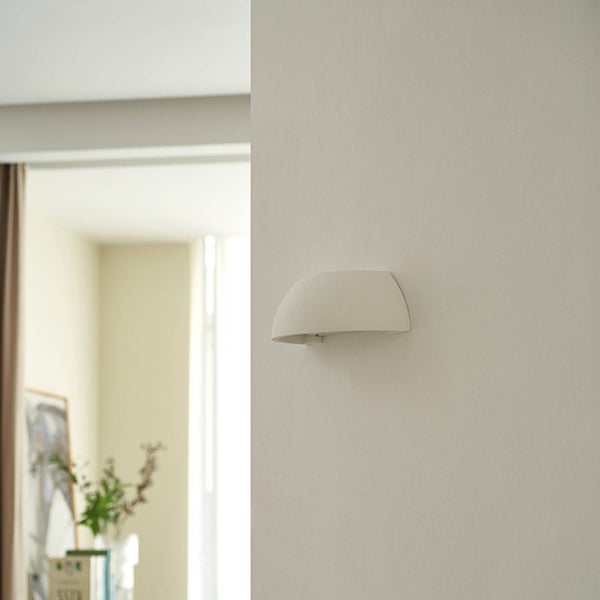 Moderne weiße gebogene Wandleuchte an einer weißen Wand in einem hellen minimalistischen Innenraum.