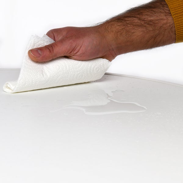 Eine Hand wischt mit einem Papiertuch eine Flüssigkeit von einer Oberfläche