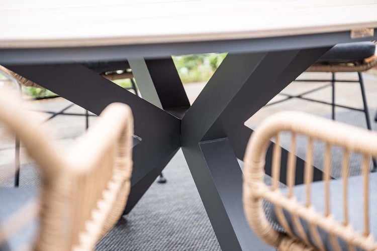 Nahaufnahme eines modernen Gartentisch-Untergestells aus anthrazitfarbenem Metall in Kreuzform mit Gartenstühlen in Korboptik.