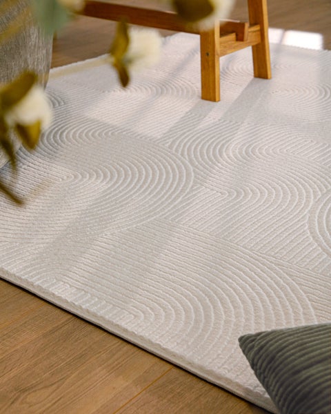 Strukturierter Teppich mit geprägtem Muster aus Kreisen und Wellen auf einem Holzboden.