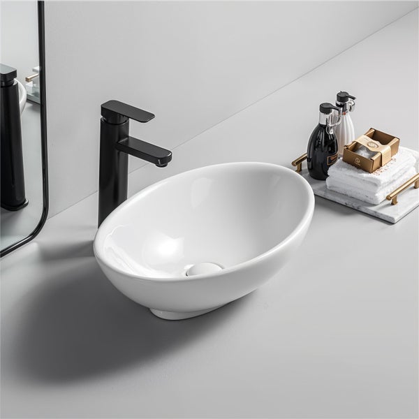 Modernes ovales Aufsatzwaschbecken aus Keramik mit schwarzer Armatur, Handtüchern und Seifenspendern in einem hellen Badezimmer.