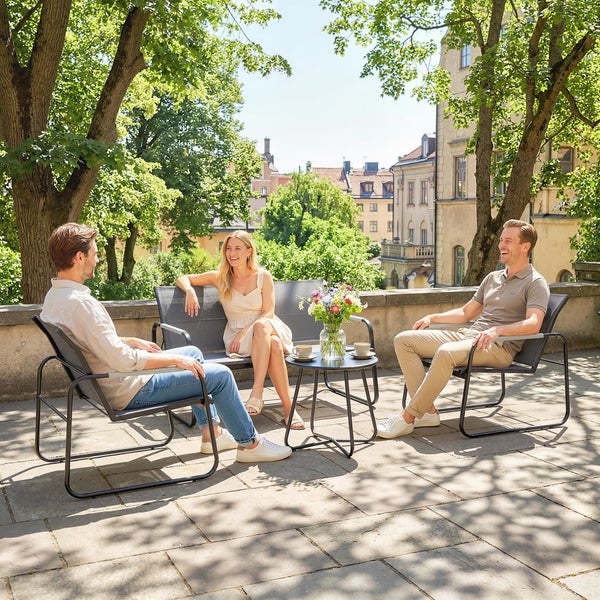 Modernes Gartenmöbel-Set aus Metall mit Bank, zwei Stühlen und Beistelltisch auf einer sonnigen Terrasse mit Bäumen und Häusern.