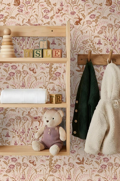 Vliestapete mit Blumen, Rehen und Hasen in einem Kinderzimmer hinter einem Holzregal mit Spielzeug und einer Garderobe.