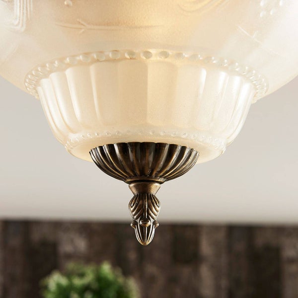 Nahaufnahme eines Lampenschirms aus satiniertem Glas mit reliefartigen Mustern und einer dekorativen Metallspitze in Bronzeoptik.