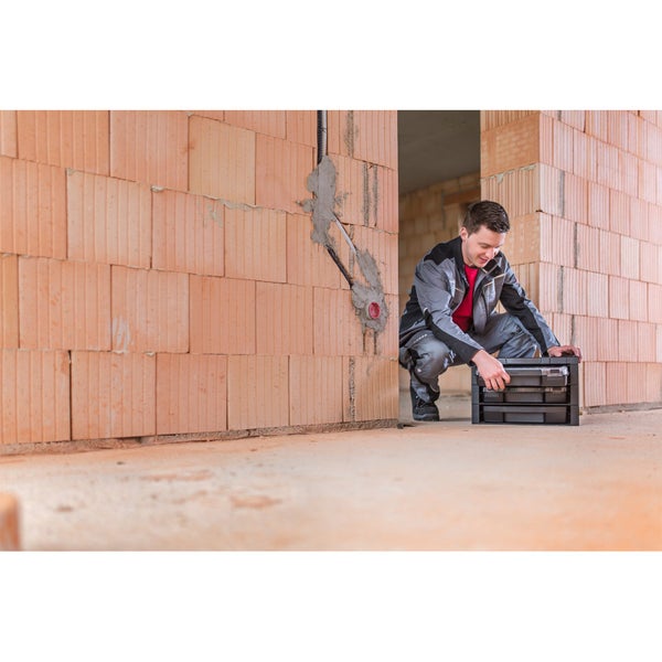 Handwerker mit Werkzeugkoffer auf einer Baustelle vor einer Ziegelwand