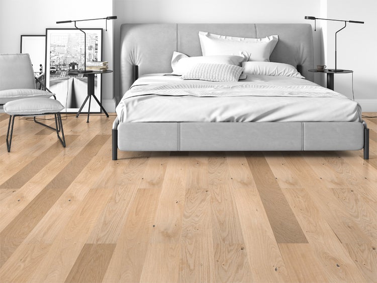 Modernes, helles Schlafzimmer mit Eiche-Landhausdielen, einem grau gepolsterten Bett und einem Sessel.