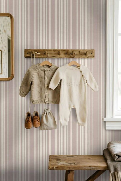 Tapete mit dezentem Streifenmuster in einem Kinderzimmer mit einer hölzernen Garderobenleiste und aufgehängter Babykleidung an der Wand.