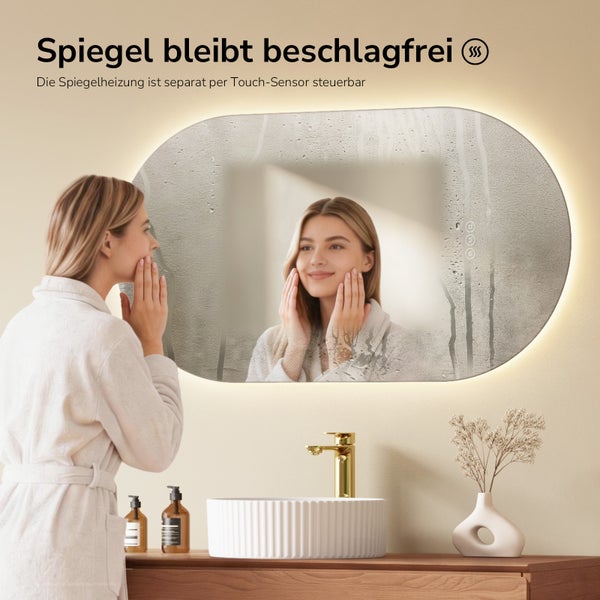 Ovaler LED-Badspiegel mit Heizfunktion und Touch-Sensor. Eine Frau im Bademantel betrachtet ihr Spiegelbild im beschlagfreien Bereich.