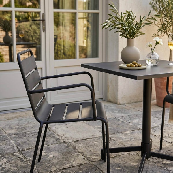 Moderner Gartenstuhl und Bistrotisch aus schwarzem Metall auf einer Steinterrasse vor einer Glastür.