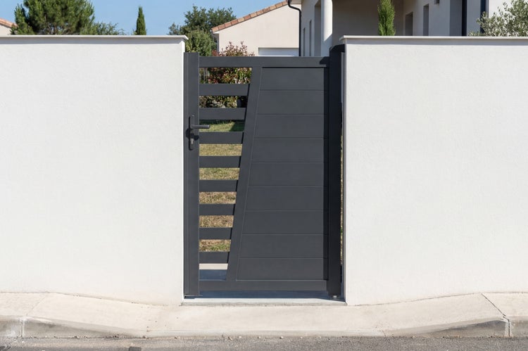 Modernes Gartentor aus Aluminium in Anthrazit mit waagerechten Lamellen und teilweiser Durchsicht, eingebaut in eine weiße Mauer.