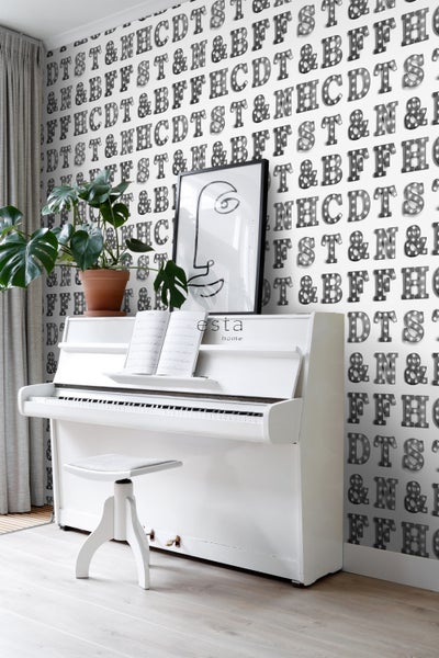Szene mit weißem Klavier, Hocker, Zimmerpflanze, abstrakter Zeichnung und Tapete mit Buchstabenmuster