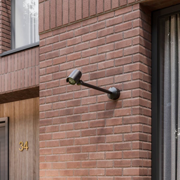 Verstellbarer Außenwandstrahler aus schwarzem Metall mit langem Arm, montiert an einer Ziegelwand.