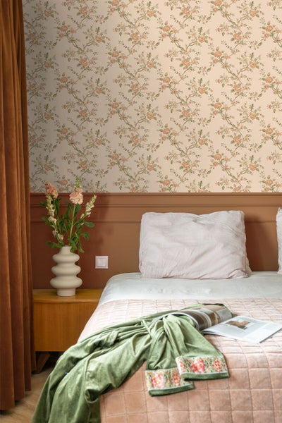 Schlafzimmer mit floral gemusterter Tapete, Wandpaneelen, Bett mit Kissen und Decke, Nachttisch mit strukturierter Vase und Blumen.