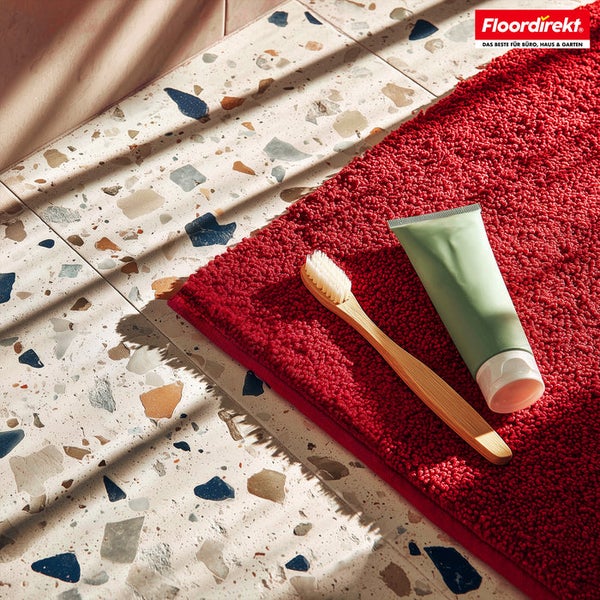 Rote Badematte mit Zahnbürste und Tube auf einem Badezimmerboden