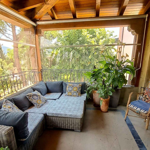 Organisierter Outdoor-Loungebereich auf Terrasse mit Holzdach, Geflecht-Ecksofa, großen Pflanzen und transparenten Wetterschutzrollos.
