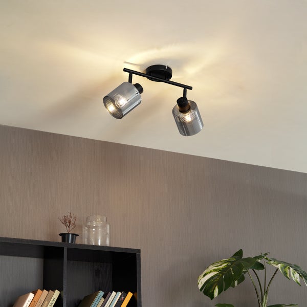 Moderner Deckenstrahler 2-flammig, schwarzes Metallgestell, geriffelte Glasschirme, montiert in einem Wohnzimmer mit Regal und Pflanze.