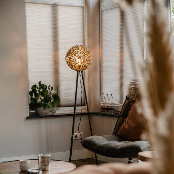 Dekorative Stehlampe mit rundem Lampenschirm und Stativfuß in einem Wohnzimmer.