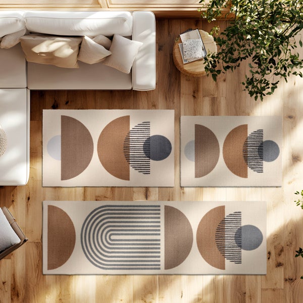 Drei Teppiche mit geometrischen Mustern auf Holzboden in einem hellen Wohnzimmer mit weißem Sofa und Pflanze, Draufsicht.