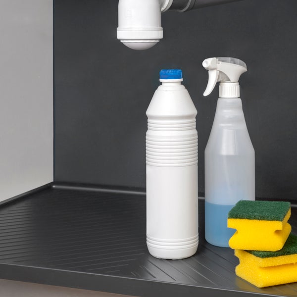 Schutzmatte für den Spülenunterschrank mit Reinigungsmitteln, Sprühflasche und Schwämmen unter einem Siphon.