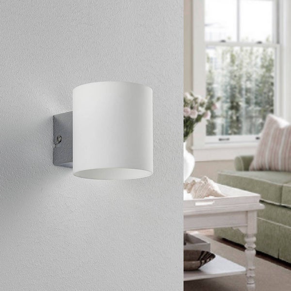 Zylindrische Wandleuchte aus Gips in Weiß, montiert an einer Wand in einem hellen Wohnzimmer mit Sofa und Tisch.